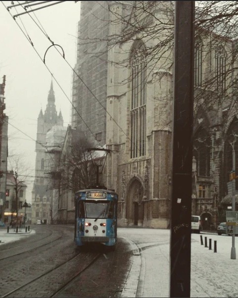 A blue tram on a snowy street beside a Gothic stone church